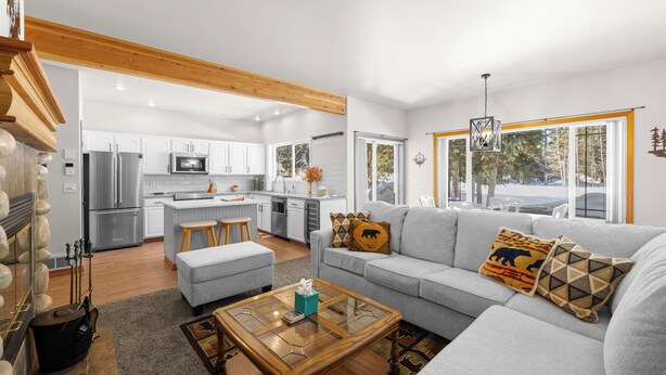 Eine moderne Küche mit weißen Schränken und Edelstahlgeräten, ein graues Sofa mit gemusterten Kissen und ein Holztisch.