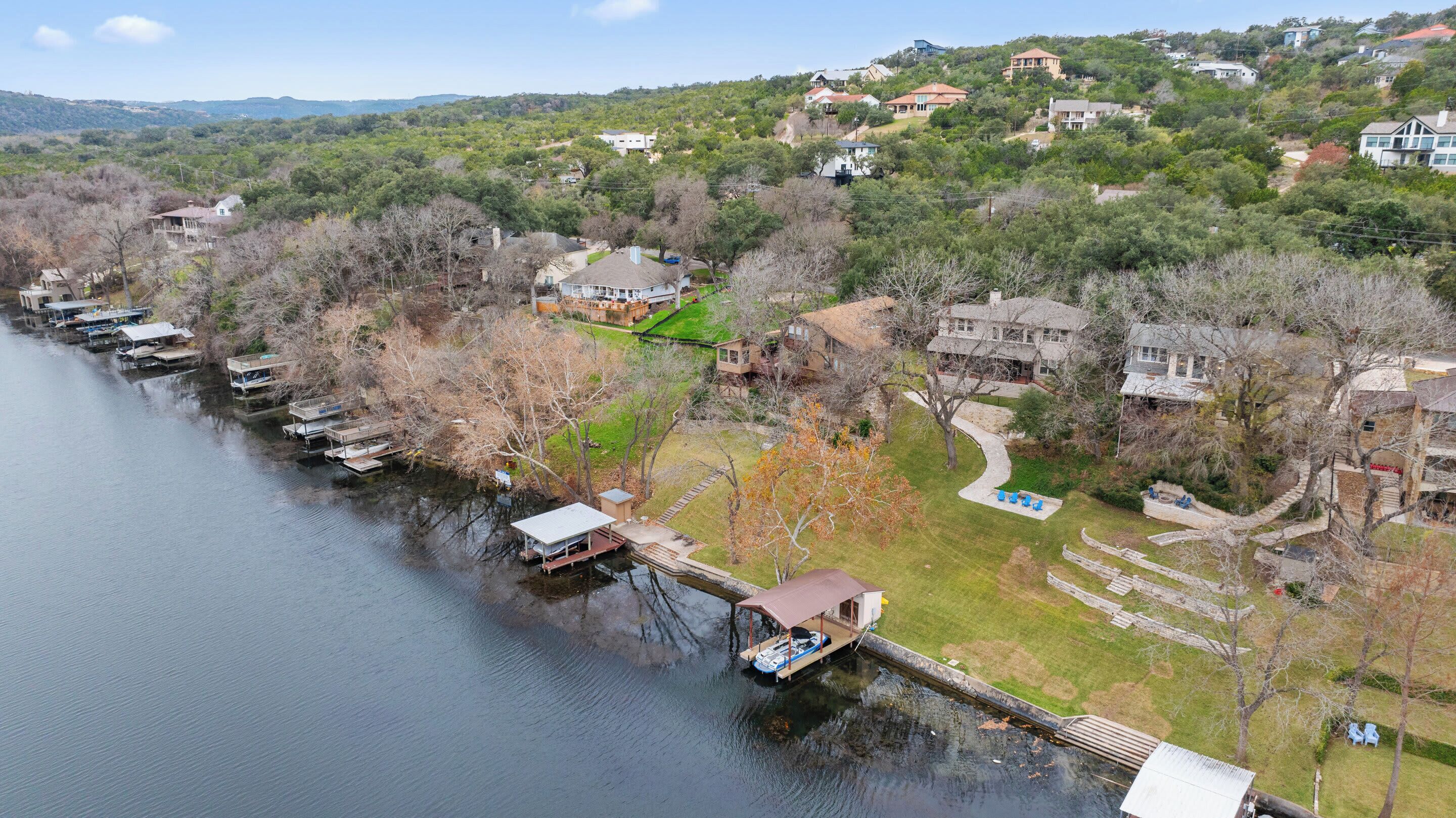 A lakeside property with docked boats, a grassy area, and houses on a hillside.