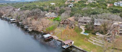 A lakeside property with docked boats, a grassy area, and houses on a hillside.