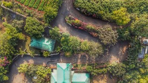 An aerial view of a property with a central building featuring a green roof, surrounded by landscaped gardens and pathways. - Amore Villa (Mahabaleshwar)