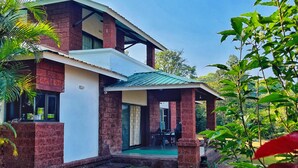 A two-story house with a brick facade, a covered porch, and a well-maintained lawn. - Amore Villa (Mahabaleshwar)