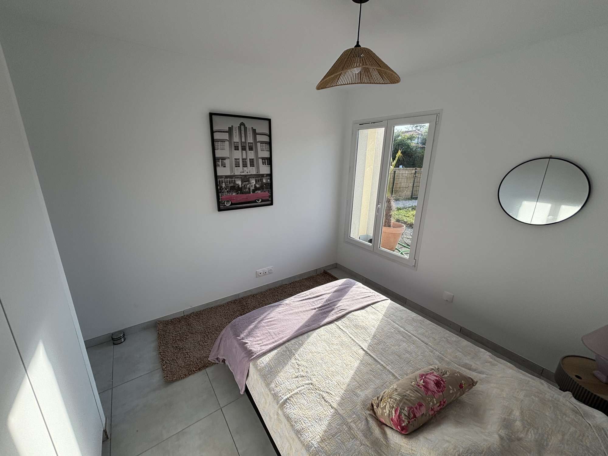 Un dormitorio con una cama, una ventana, una lámpara colgante y un espejo instalado en la pared.