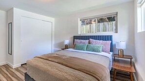 Une chambre à coucher avec un lit, une table de chevet, une fenêtre donnant sur une clôture en bois et une porte.