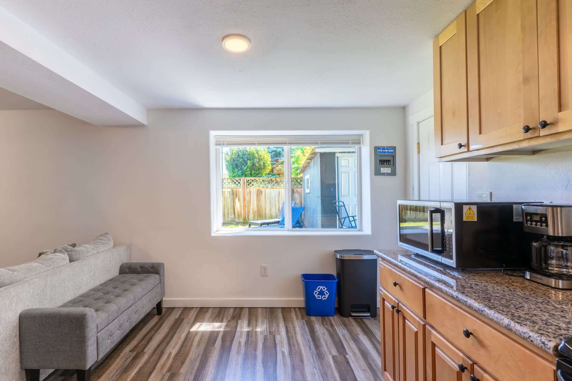 A compact kitchen with wooden cabinets, a microwave, and a trash bin.