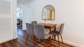 Un coin repas avec une table en bois, quatre chaises grises et un grand miroir au mur.