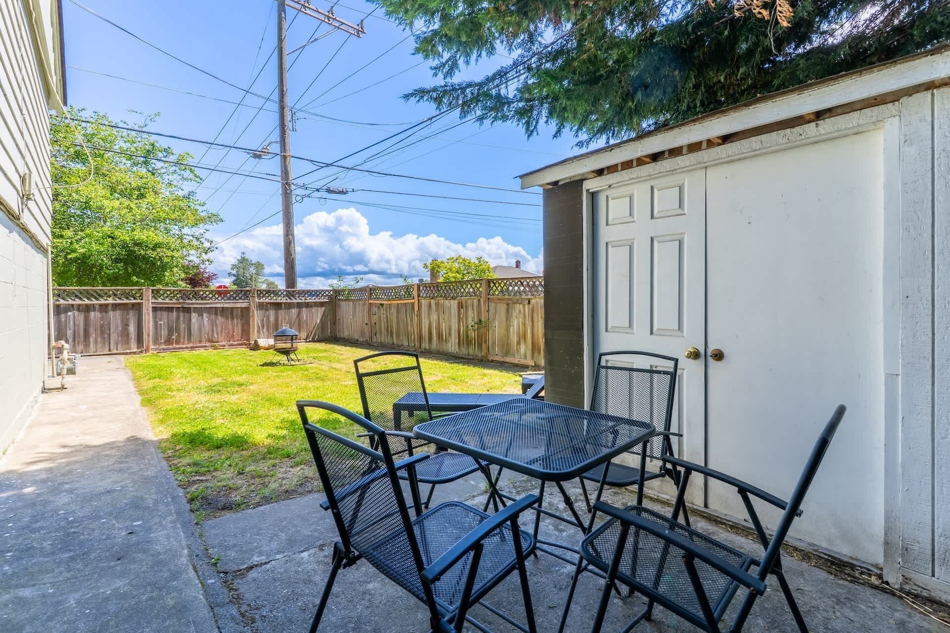 Une cour arrière avec une table et des chaises en métal, une clôture en bois et une porte de garage.