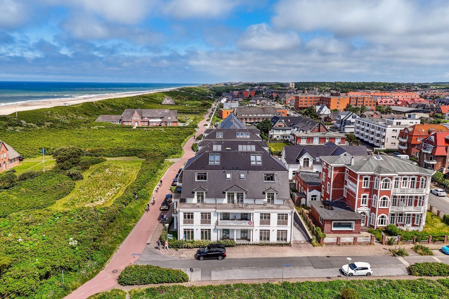 Un pueblo costero con un edificio destacado de techo pronunciado y balcón, rodeado de casas residenciales y una playa al fondo.