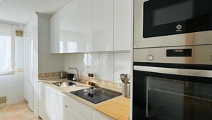 A modern kitchen with white cabinets, a black oven, and a stainless steel range hood. - Millenium Apartment (Redondela)