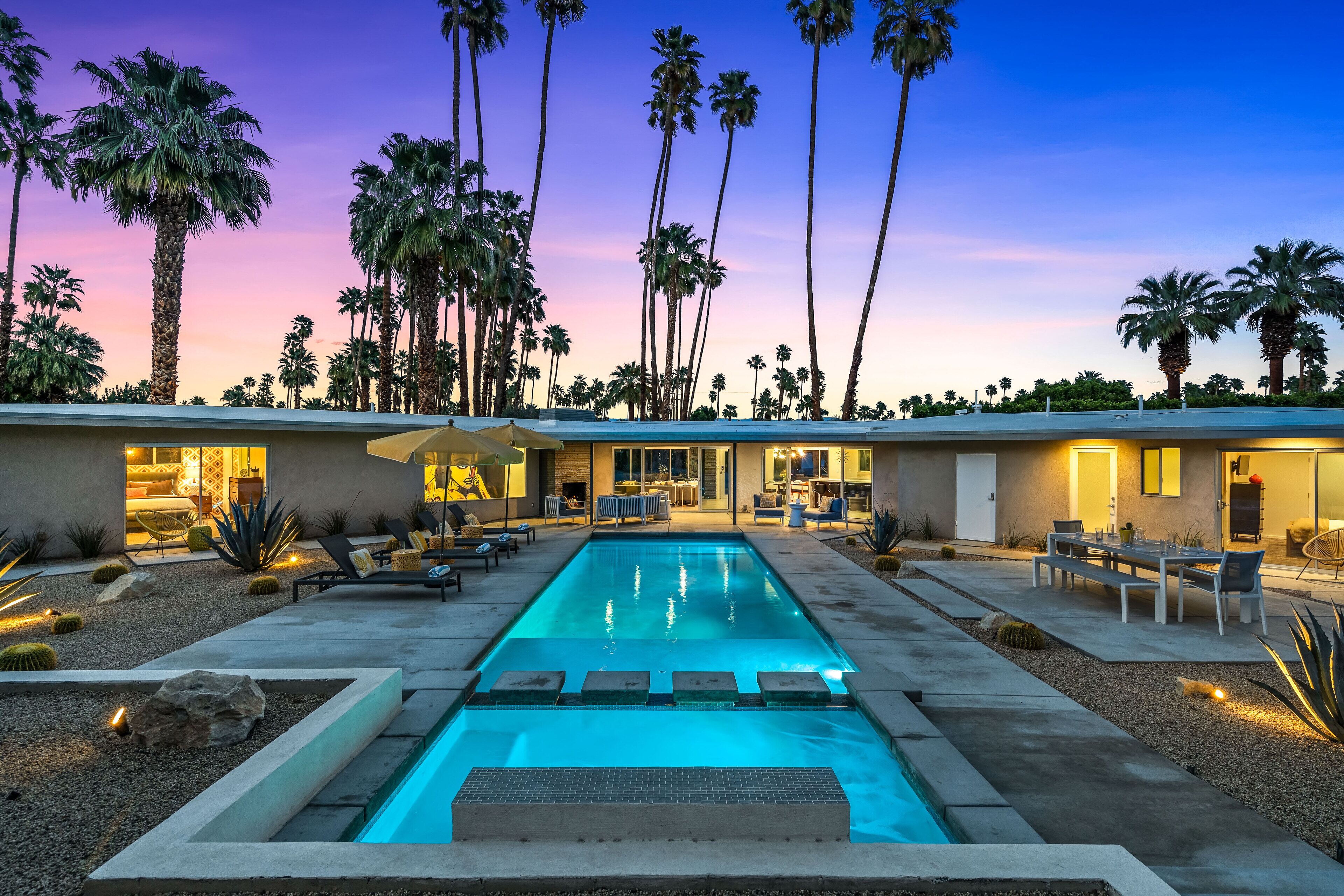 A modern pool area with a rectangular pool, lounge chairs, and a dining area with outdoor furniture.