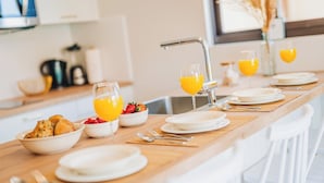 A breakfast setup with bowls of cereal and fruits, plates, and glasses of orange juice on a wooden table.