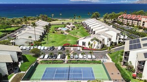 Un resort con varias construcciones, una cancha de tenis y una piscina.
