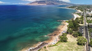 Vista aérea de una zona costera con playa, una montaña y una carretera con edificios.
