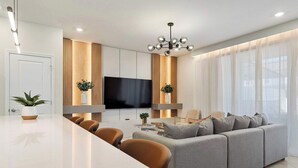 Una sala de estar moderna con un sofá gris, sillas marrones, un televisor de pantalla plana y un ventanal con cortinas ligeras.