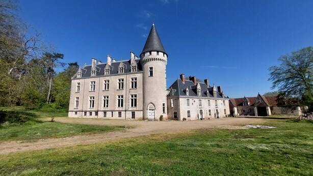 Un castillo grande e histórico con una torre destacada, rodeado de jardines bien cuidados y un cielo despejado.