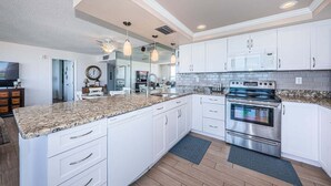 Una cocina moderna con armarios blancos, encimeras de granito, electrodomésticos de acero inoxidable e iluminación colgante.