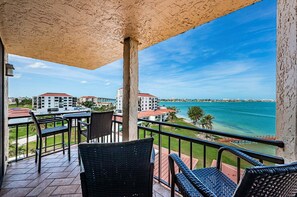 Een balkon met rieten meubilair, uitzicht op de oceaan en gebouwen op de achtergrond.