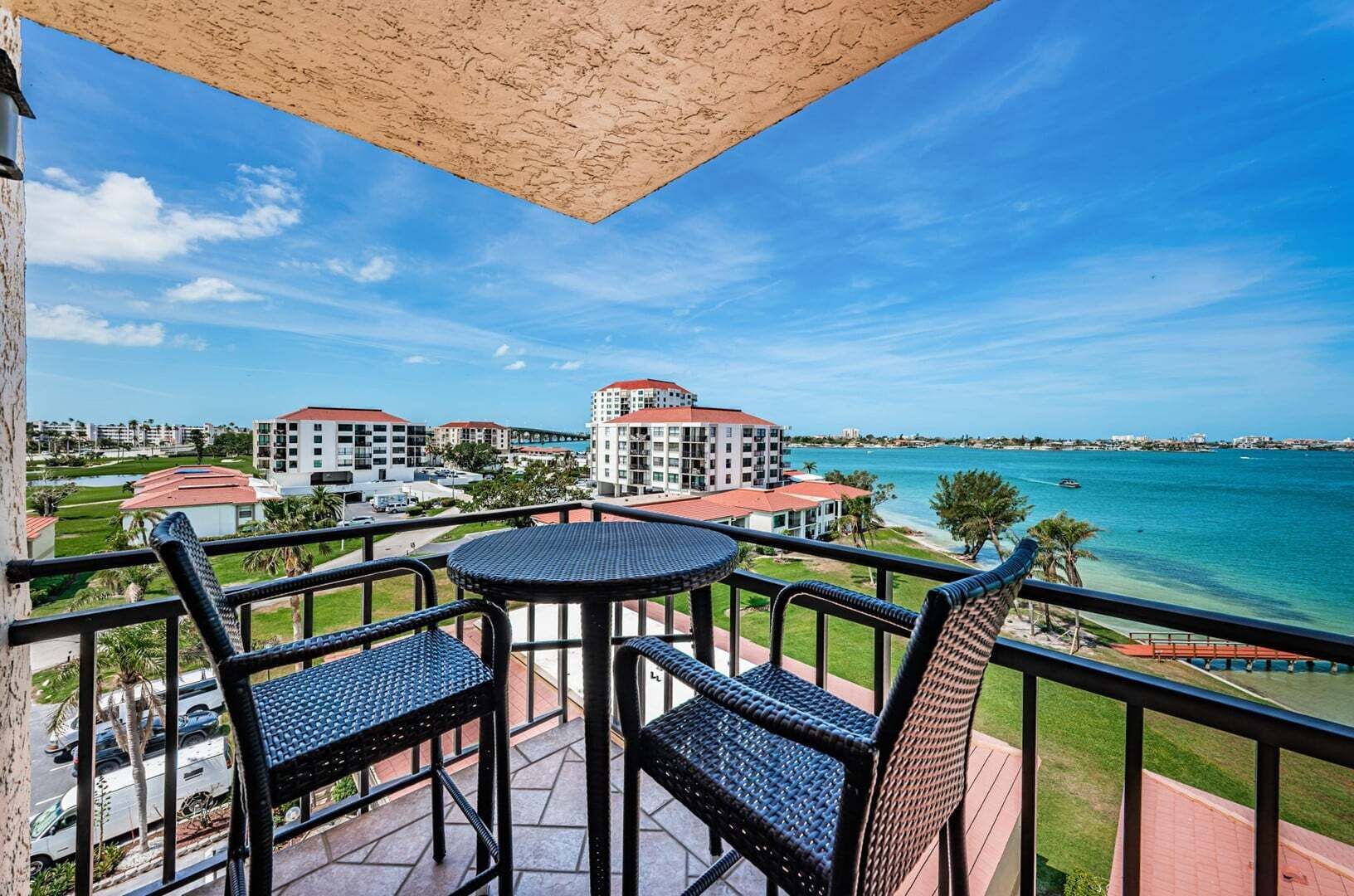 Ein Balkon mit Tisch und Stühlen, der auf eine Küstenlandschaft mit Gebäuden und blauem Himmel blickt.