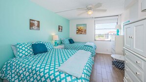 Una habitación con dos camas, ventilador de techo, ventana con vistas y cómoda.