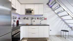 A modern kitchen with white cabinetry, a stainless steel refrigerator, a microwave, and a gas stove. There is a small island with a sink and a decorative wall piece above it. - Tenerife Royal Gardens 23 - One Bed (Playa de las Américas)