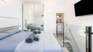 A modern bedroom with a bed, a large mirror, a TV, and a glass-enclosed shower area. - Tenerife Royal Gardens 23 - One Bed (Playa de las Américas)