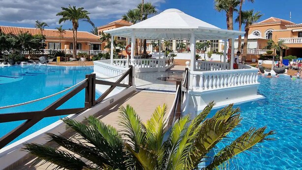 A resort pool area with a gazebo, palm trees, and a clear blue sky. - Tenerife Royal Gardens 23 - One Bed (Playa de las Américas)