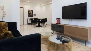 Un saló modern amb televisió de pantalla plana, zona de menjador amb taula i cadires, i un sofà amb una taula de centre.