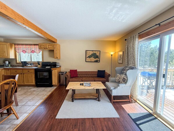 Una sala acogedora con piso de madera, un sofá, una mesa de centro, una mesa de comedor y una cocina con gabinetes de madera y una estufa.