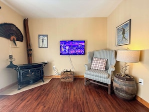 Una habitación con piso de madera, un sillón escocés, una lámpara antigua, un televisor y un cuadro en la pared.