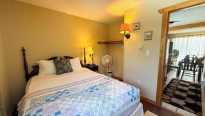 A bedroom with a bed, two bedside lamps, a wall-mounted fan, and a view of a dining area through an open door. - Alpine Horn #2 ~ Sauna & Close to Powderhorn! (Bessemer)
