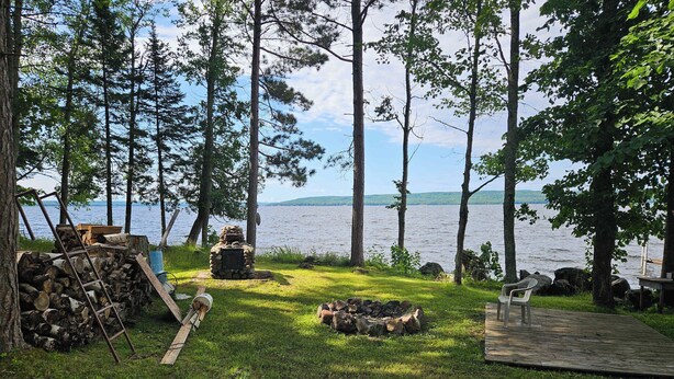 Un espace extérieur aménagé au bord du lac, avec un foyer, une pile de bois de chauffage et une terrasse en bois.