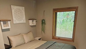 Une chambre à coucher avec un lit, une fenêtre avec des stores, une plante suspendue et une étagère fixée au mur.
