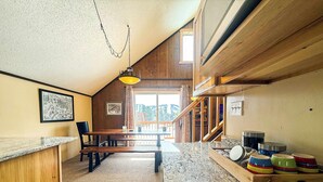 A cozy kitchen with wooden accents, a marble countertop, and a dining area with a table and chairs. - Alpine Horn # 1 ~ Sauna & Close to Powderhorn! (Bessemer)