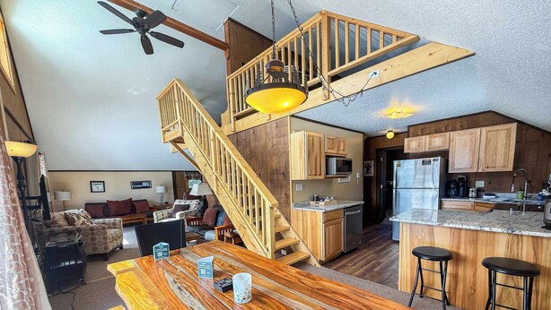 A spacious living area with a wooden staircase, a kitchen with modern appliances, and a dining area with a large wooden table. - Alpine Horn # 1 ~ Sauna & Close to Powderhorn! (Bessemer)