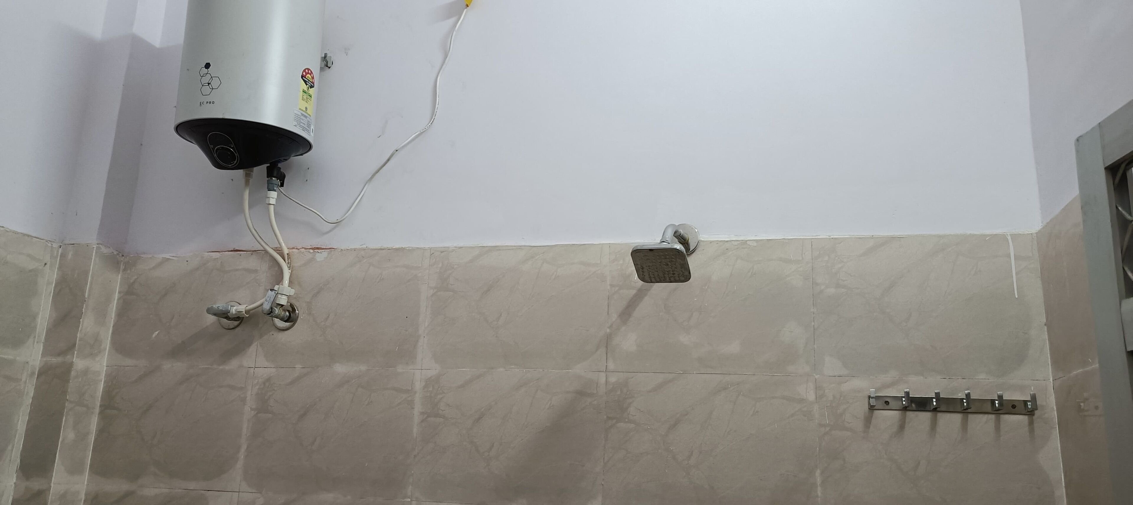 Un baño con calentador de agua instalado en la pared, un cabezal de ducha y suelo de baldosas.
