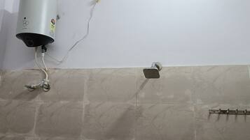 Un baño con calentador de agua instalado en la pared, un cabezal de ducha y suelo de baldosas.