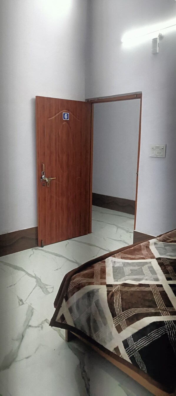A room with a wooden door marked with the number 6, a tiled floor, and a bed with a patterned bedspread.