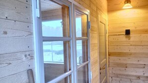 A wooden interior with a large window, a door, and a wall-mounted light fixture. - Viltpark Rollerbü Hjortaröd (Tyringe)