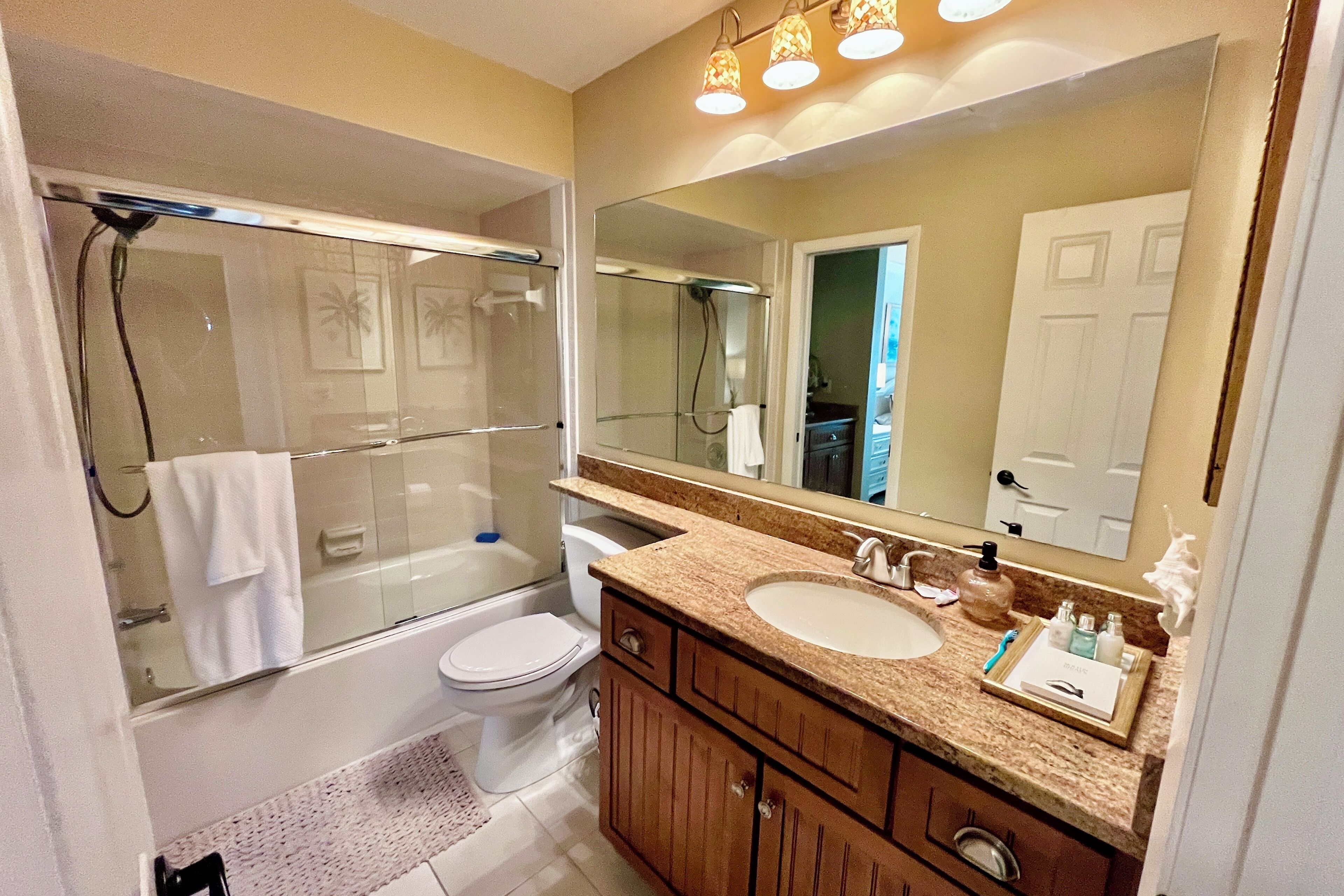 A bathroom with a glass-enclosed shower, a toilet, a sink with a vanity, and a large mirror.