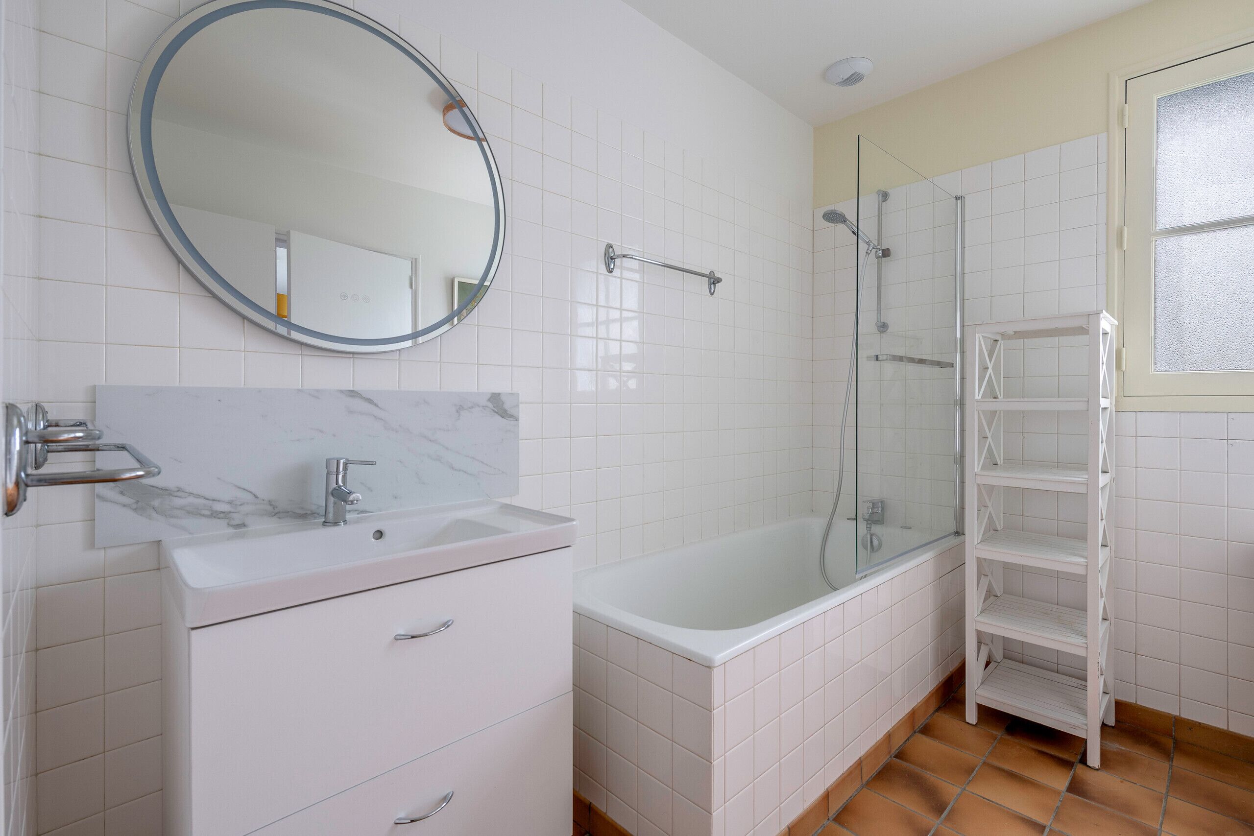 A modern bathroom with a white vanity, a large mirror, a bathtub, and a glass-enclosed shower.