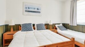 A room with two wooden beds, each with a white duvet and patterned pillows. There is a wooden nightstand with a lamp on each side of the beds. A painting hangs on the wall above the beds, and a window with striped curtains is visible. - House for 10 with garden in Noirmoutier (Noirmoutier-en-l´Ile)