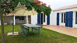 A patio area with a table and chairs, a covered seating area, and a building with blue shutters. - House for 10 with garden in Noirmoutier (Noirmoutier-en-l´Ile)