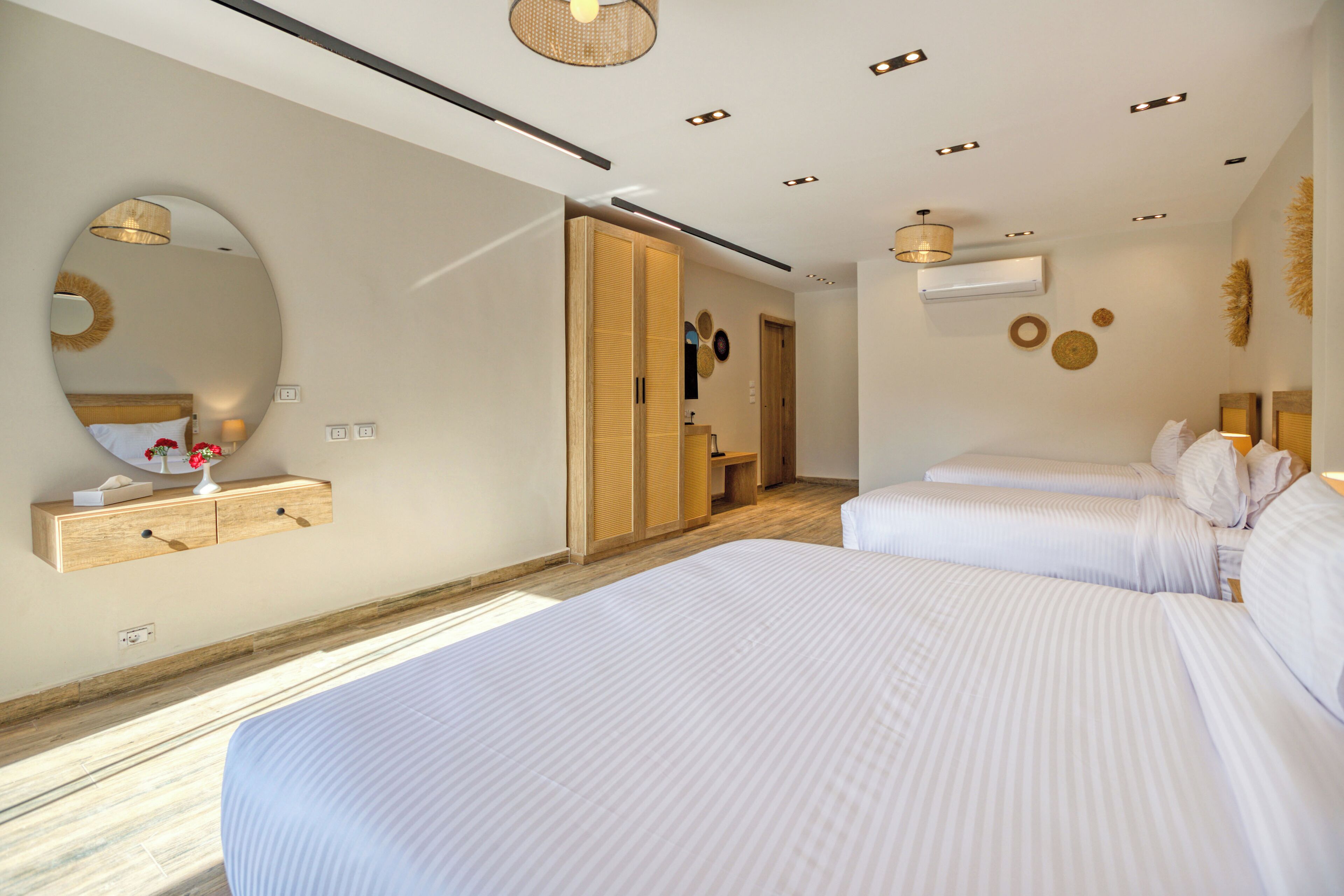 Una habitación de hotel moderna con dos camas, un espejo grande, un armario y un baño pequeño.