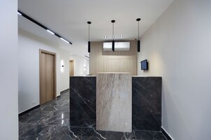 A modern hallway with a marble floor, a wooden door, and a reception desk with a flat-screen TV.