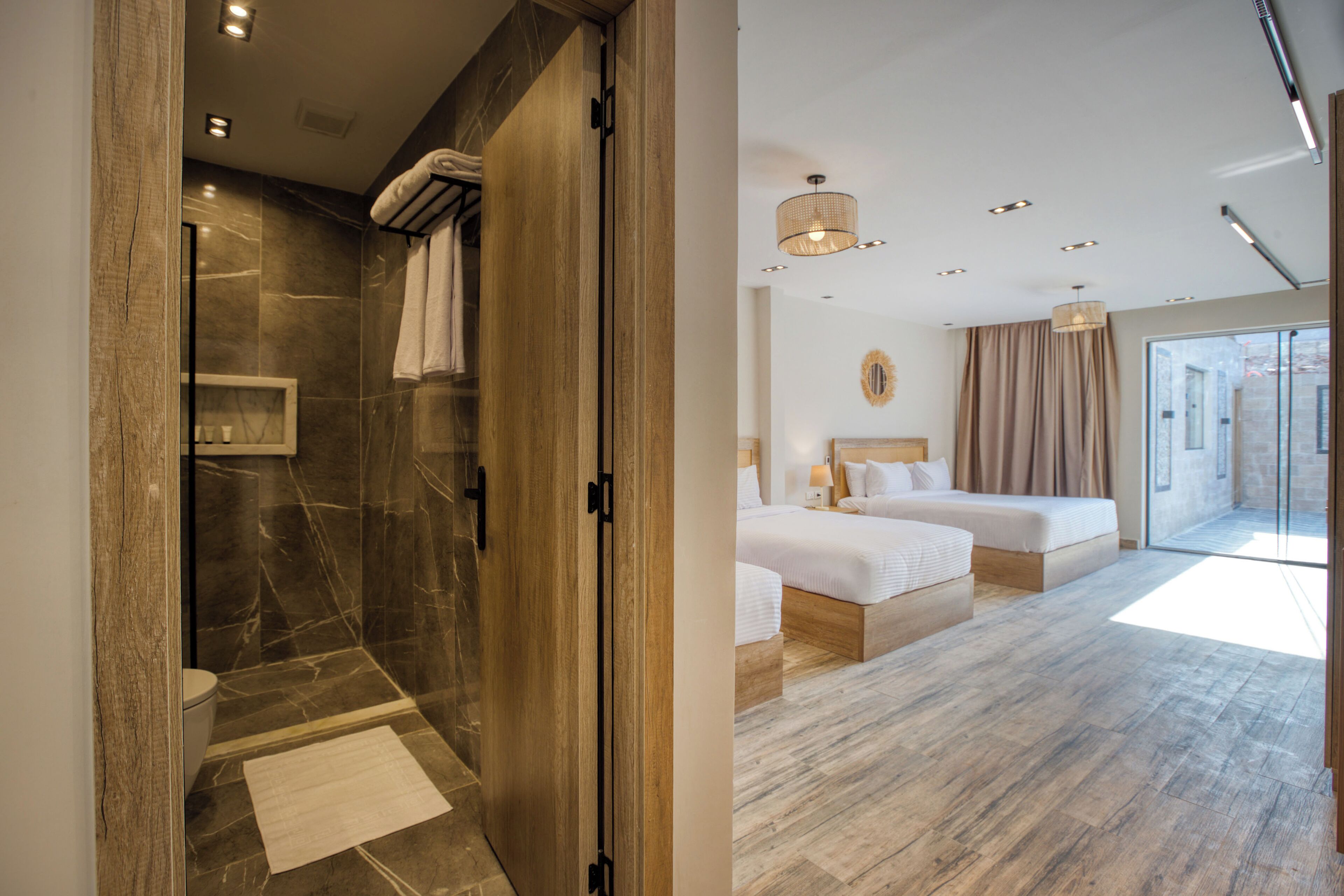 A modern hotel room with a shower area, a bed, a bedside table, and a view of the outside.