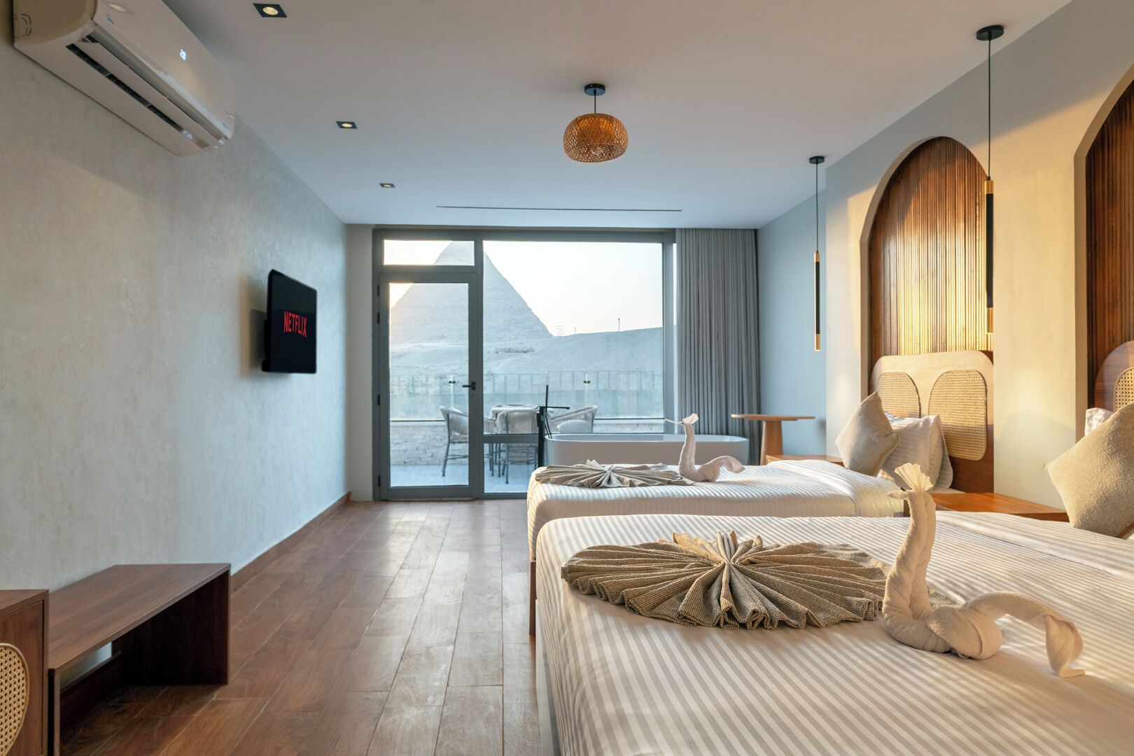 A hotel room with two beds, a TV, a balcony with a table and chairs, and a view of a mountainous landscape.