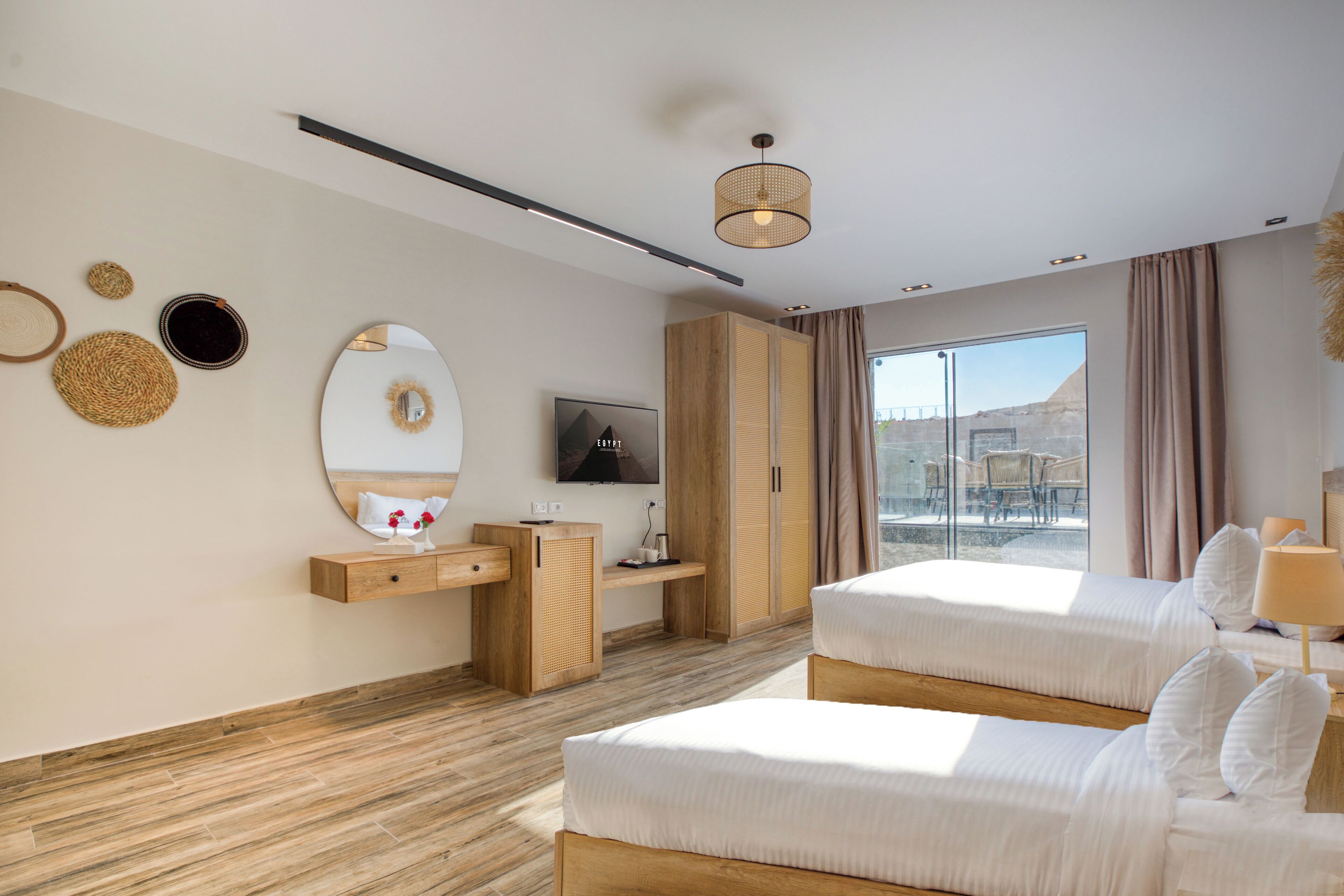 Habitación de hotel moderna con dos camas, un televisor, un escritorio de madera y un ventanal con vistas.