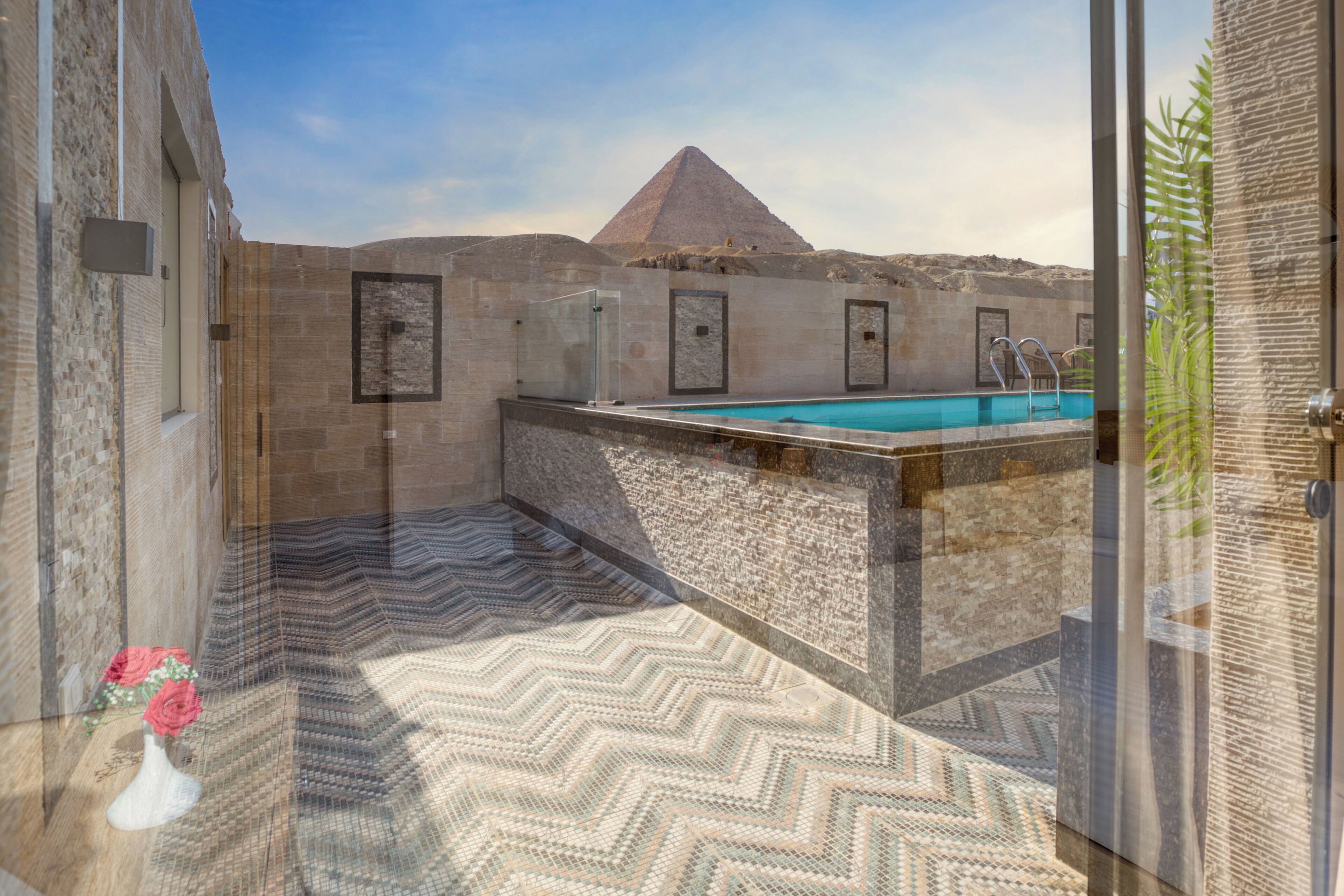Ein Pool auf dem Dach mit Blick auf die Pyramide, umgeben von Steinmauern und einem gemusterten Boden.