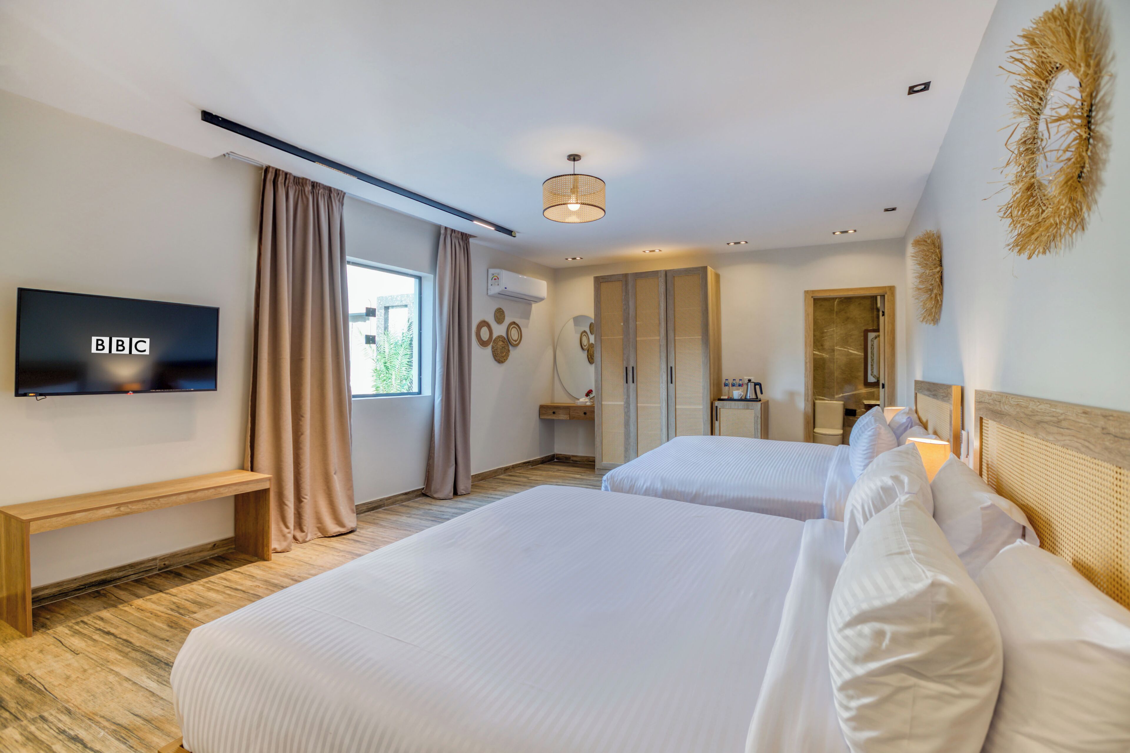A hotel room with two beds, a TV, a bathroom, and a large window.