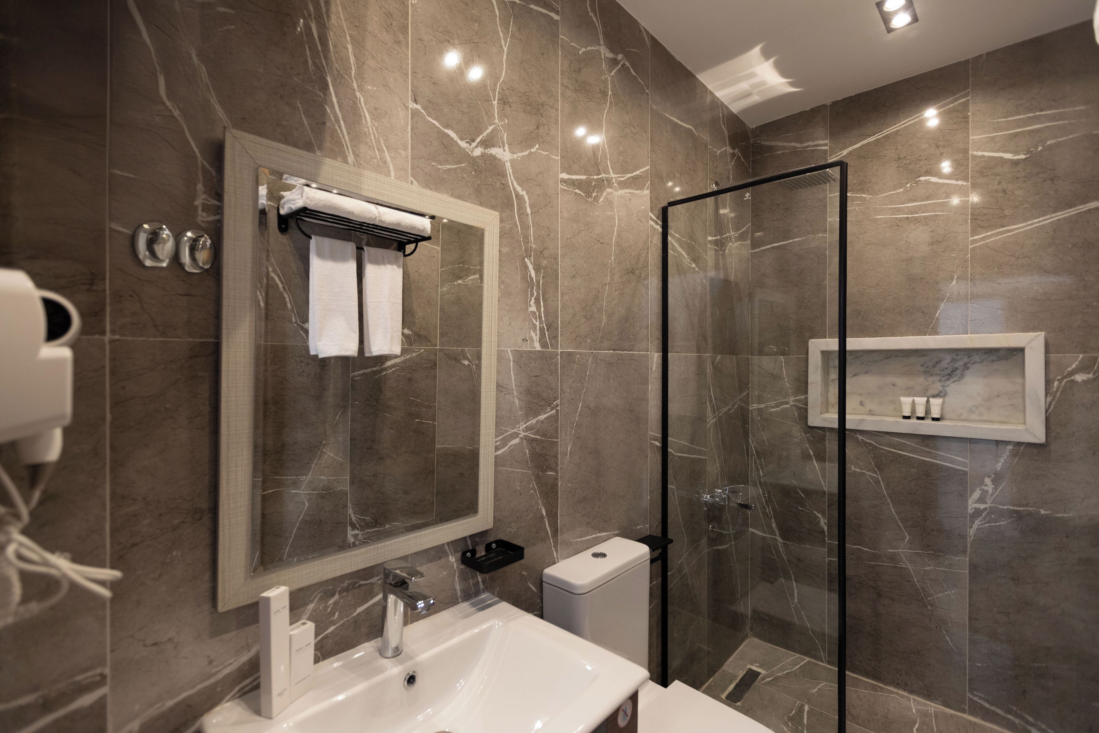 A modern bathroom with a marble sink, a glass shower enclosure, and a built-in shelf with toiletries.