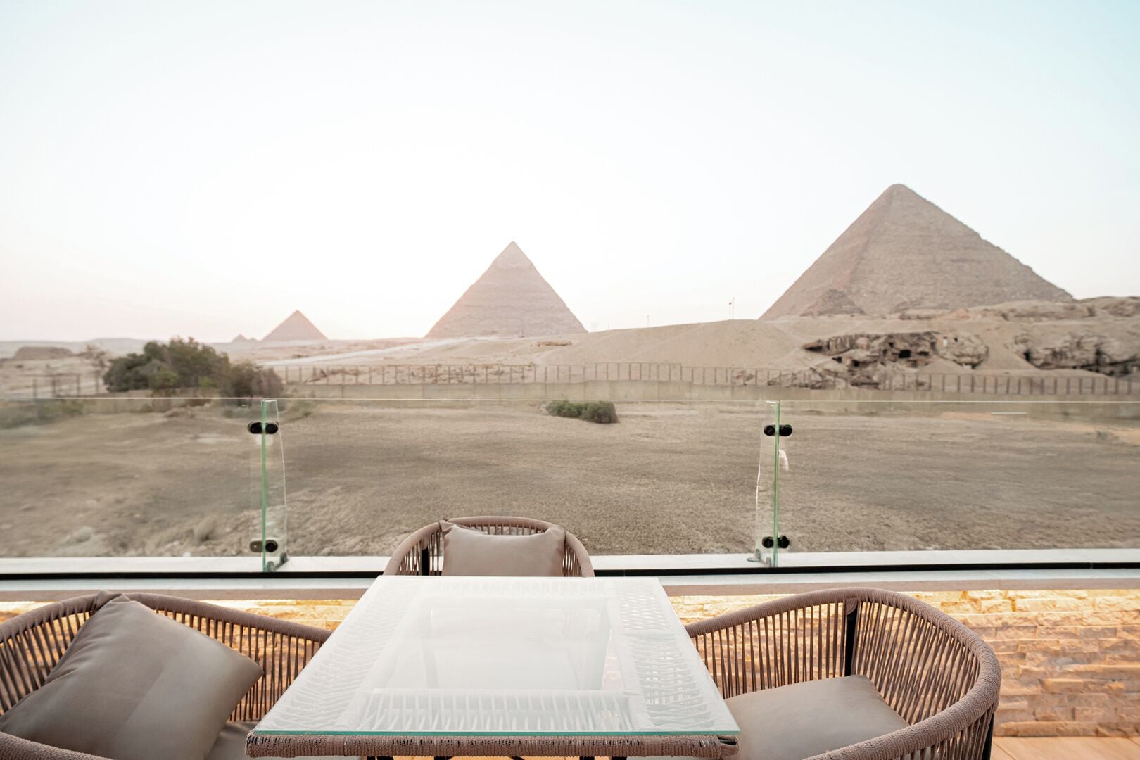 A balcony with wicker chairs and a table, overlooking the pyramids.